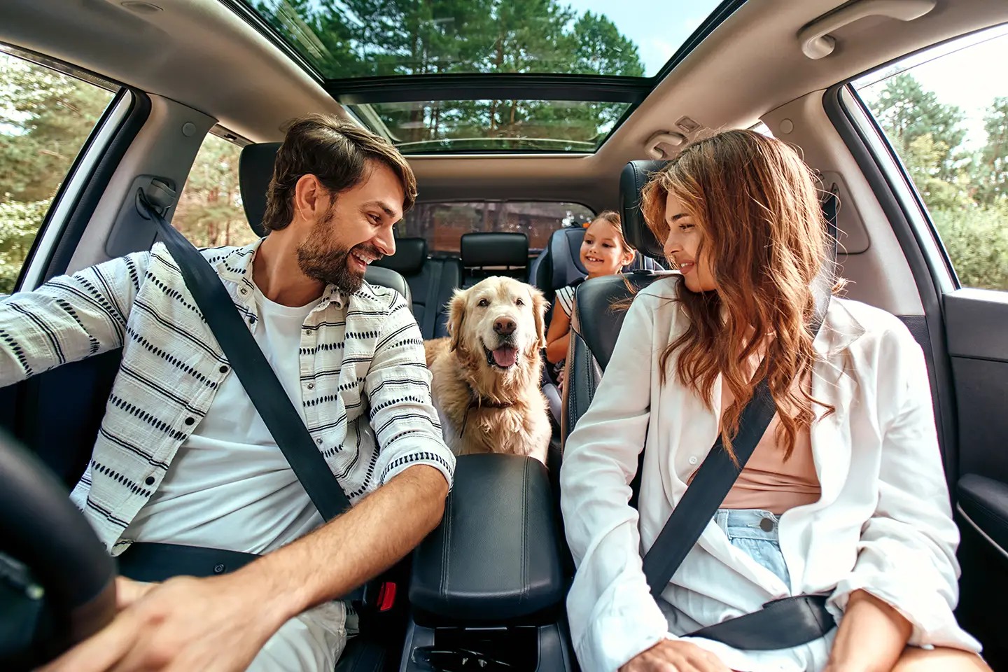 A happy family, mum, dad and daughter in their car with their dog about to go on a journey.